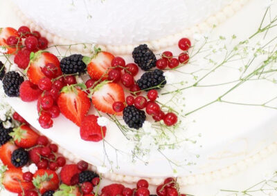 Torta nuziale su tre piani decorata con della frutta fresca e dei fiori.