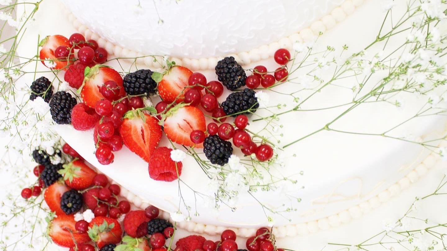 Torta nuziale  su tre piani decorata con della frutta fresca  e dei fiori.